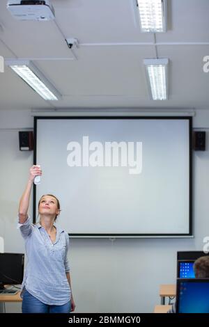 Jolie, jeune enseignante dans une salle de classe, prêt à enseigner une classe, préparer un projecteur Banque D'Images