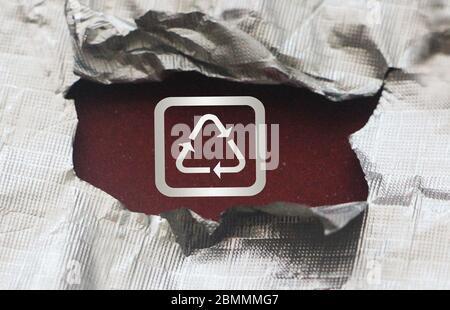 Symbole de recyclage en argent sur le rouge foncé sous le papier d'aluminium déchiré. ECO vie saine réutilisation réduire concept Banque D'Images