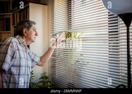 COVID-19 quarantaine de la santé mentale. Homme âgé regardant sur la fenêtre, isolement, solitude, distance sociale Banque D'Images