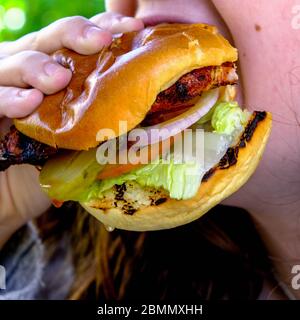 Anonyme jeune femme manger UN savoureux hamburger de poulet frais dans UN Bun de brioche grillé Banque D'Images