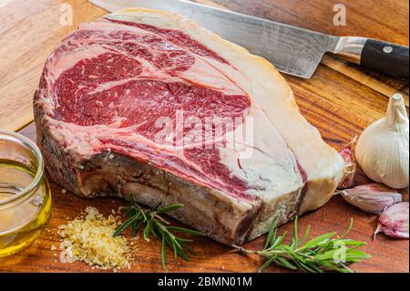 Steak de gallega vaca rubia vieilli, prêt à être grillé avec de l'ail, du romarin, des flocons de sel et de l'huile d'olive extra vierge et un couteau de cuisine sur une table en bois Banque D'Images