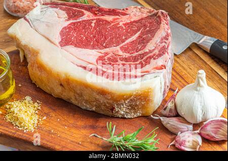 Steak de gallega vaca rubia vieilli, prêt à être grillé avec de l'ail, du romarin, des flocons de sel et de l'huile d'olive extra vierge et un couteau de cuisine sur une table en bois Banque D'Images