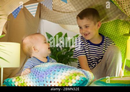 Deux frères mignons jouent avec une lampe de poche dans une tente pour enfants. garçon et bébé de 6 ans Banque D'Images