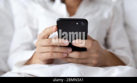 Gros plan des mains de femmes tenant un smartphone noir allongé dans le lit Banque D'Images