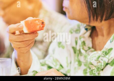 Un morceau de pastèque dans la main d'une vieille femme tout en parlant à un dîner-fête. Banque D'Images