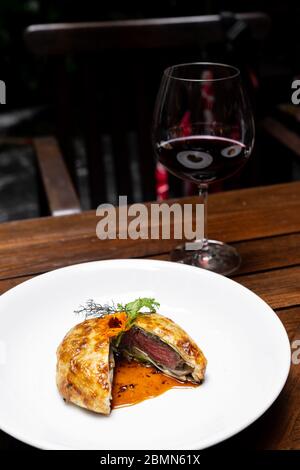Bœuf rôti Wellington avec sauce sauce brune salée, cuisine gastronomique internationale de viande de bœuf farinée dans une purée de pain cuite au four avec un verre de vin rouge. ONU Banque D'Images