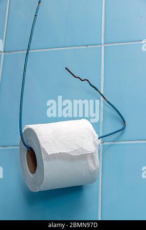 Un rouleau de papier toilette est suspendu sur un fil de fer sur un mur de tuiles bleues. Porte-papier toilette simple dans la salle de bains. Banque D'Images