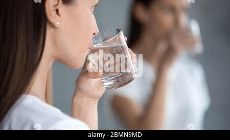 Femme réfléchissant dans le miroir debout à l'intérieur de boire de l'eau filtrée de près Banque D'Images