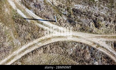 Vue aérienne d'un carrefour entre deux routes de terre dans la campagne ouverte. Un poteau souligne une longue ombre sur le sol. Banque D'Images