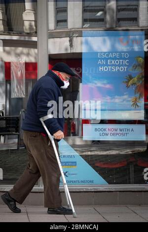 Un homme âgé sur des béquilles et portant un masque chirurgical passe devant un agent de voyage TUI à Cardiff, au pays de Galles, au Royaume-Uni Banque D'Images