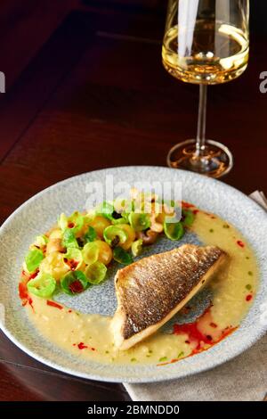 Savoureux filet de bar grillé servi avec des pousses de saumure cuites à la vapeur, des champignons rôtis, des pommes de terre, des oignons caramélisés et une sauce crémeuse, servi avec un verre de Banque D'Images