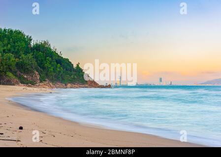 Quy Nhon panorama de la ville depuis la plage de sable célèbre destination touristique au Vietnam. Effet de longue exposition des vagues de mer douces de la baie de Quy Nhon. Lumière du coucher de soleil au-delà de sk Banque D'Images