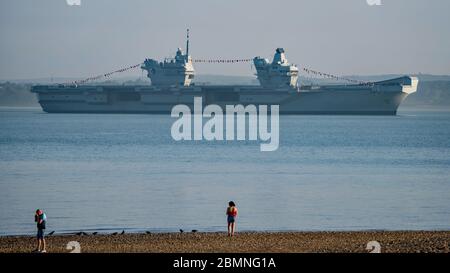 Le porte-avions de la Marine royale HMS Queen Elizabeth à l'ancre dans le Solent, au large de l'île de Wight, au Royaume-Uni, dans la soirée du 8 mai 2020. Malgré le blocage national du coronavirus, le navire est habillé de façon générale pour commémorer le 75e anniversaire de la fête de la VE. Banque D'Images