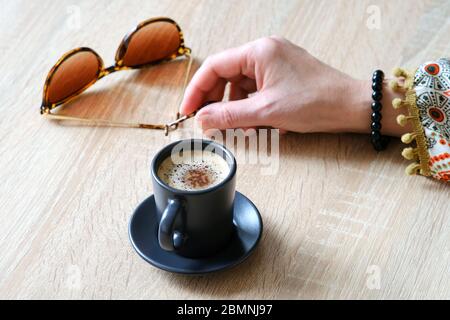 Une fille est assise dans un café, tenant une paire de lunettes de soleil dans sa main. Dans une tasse de latte, les copeaux de chocolat reposent sur la mousse Banque D'Images