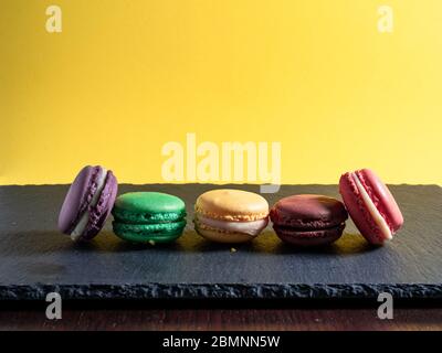 Cinq macarons de différentes couleurs disposés en rangée sur un fond jaune lisse Banque D'Images