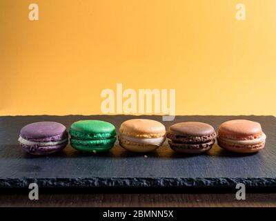 Cinq macarons de différentes couleurs disposés en rangée sur un fond orange lisse Banque D'Images