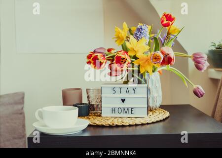 Composition confortable d'une tasse de thé, visionneuse avec message de séjour à la maison et bouquet de fleurs de printemps fraîches sur la table basse près de la fenêtre. Tout pour un Banque D'Images