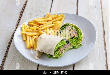 Pancake de pain pita farci de viande, laitue, poivron rouge et pommes de terre frites sur une assiette blanche, sur une table en bois. Gros plan. Banque D'Images