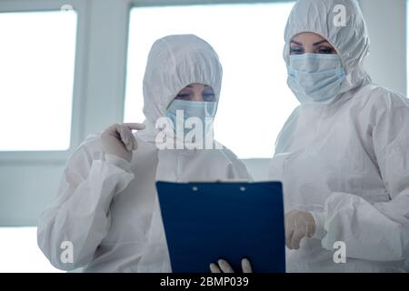 Travailleurs médicaux en vêtements de protection et masques médicaux lisant quelque chose sur le dossier de clips Banque D'Images