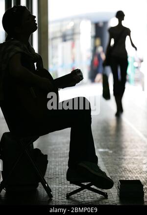 Une silhouette d'une chanteuse assise et jouant de la guitare pour les gens qui passent Banque D'Images