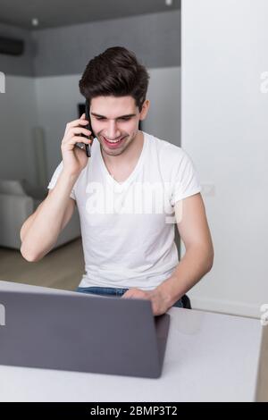 Portrait de l'homme utilisez un ordinateur portable tout en parlant au téléphone à la maison. Travailler à domicile Banque D'Images