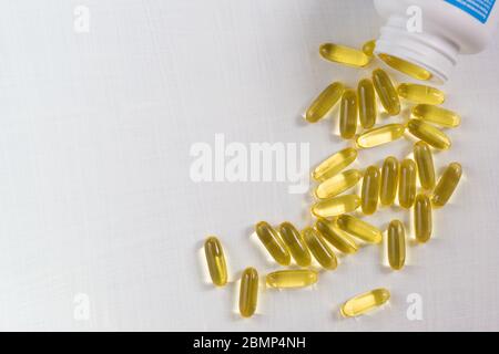 Capsules gélatineuses transparentes d'huile de poisson déversées de la bouteille sur le bord de la table blanche. Gras polyinsaturés oméga-3 essentiel a Banque D'Images