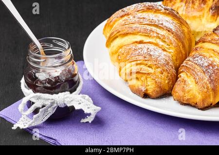 Croissants français en gros plan, jarre de confiture servie sur une serveuse pourpre. Cuisson maison à base de pâte feuilletée. Banque D'Images