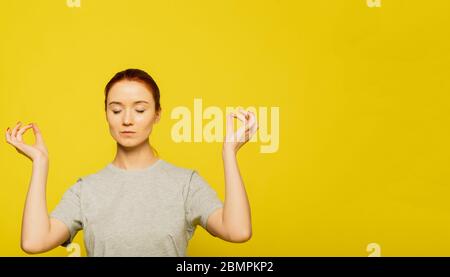 Yoga et méditation. Belle femme jeune rousse vêtue de façon décontractée, gardant les yeux fermés tout en méditant, se sentant détendue, calme et paisible après har Banque D'Images