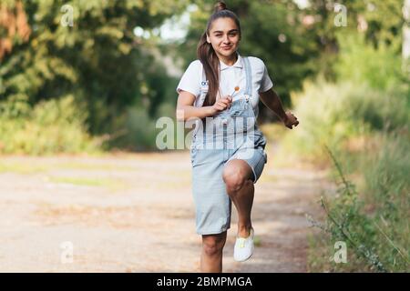 Une fille en combinaison denim sourit et court à l'extérieur. Banque D'Images