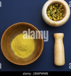 Mortier de marbre avec camomille séchée pour cosmétiques naturels. Bols en argile et en verre avec poudre jaune ou argile et fleurs. Plat, bleu classique. Banque D'Images