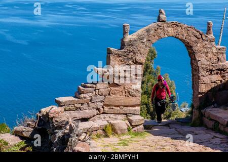 Homme péruvien local traversant une arche de pierre typique d'Isla Taquile avec le lac Titicaca en arrière-plan, île Taquile, Pérou Banque D'Images