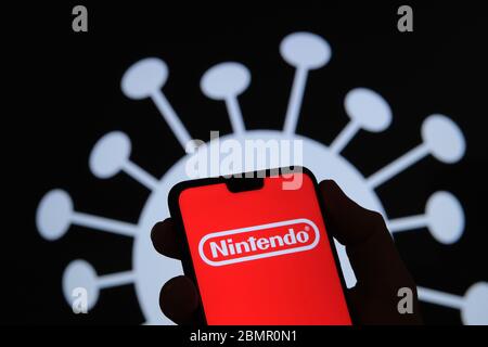 Logo de la société Nintendo sur une silhouette de smartphone tenir dans la main. Image du coronavirus sur un arrière-plan flou. Une vraie photo, pas un montage. Banque D'Images