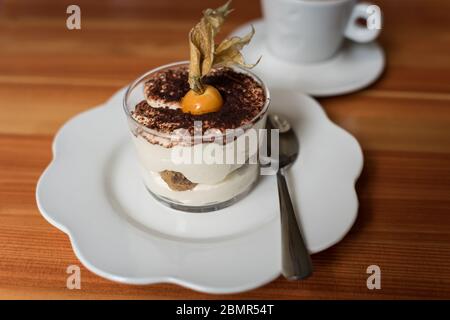 Dessert tiramisu dans un verre décoré avec des baies d'inca, des baies de physalis et une tasse de café sur le fond Banque D'Images