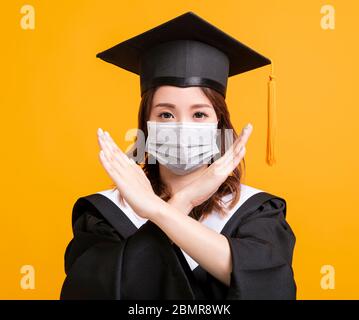 jeune femme en remise de diplôme avec masque médical et montrant stop geste Banque D'Images