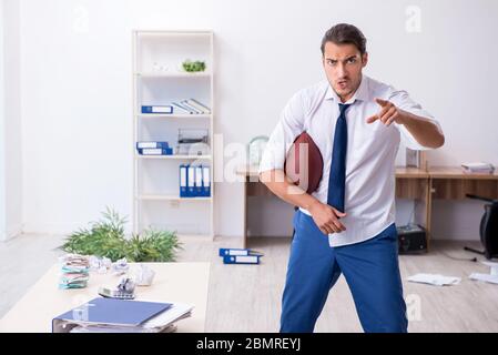 Jeune employé jetant du ballon de rugby dans le bureau Banque D'Images