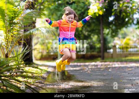 Enfants jouant dans la pluie dans le parc d'automne. Enfant sautant dans une flaque boueuse le jour de l'automne pluvieux. Petite fille en bottes de pluie et veste arc-en-ciel à l'extérieur à Tseindeideà Banque D'Images