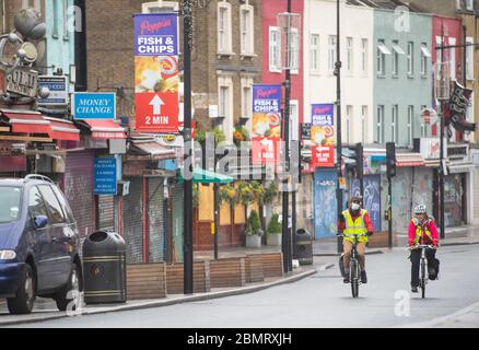 Les cyclistes se trouvent à proximité des magasins à volets de Camden High Street, dans le nord de Londres. Les destinations commerciales ont vu leur plus grand déclin jamais enregistré le mois dernier, alors que les acheteurs séjournaient chez eux dans le cadre de la pandémie du coronavirus, selon de nouveaux chiffres. Banque D'Images