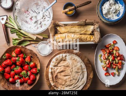 Préparation de gâteau de wrap de rhubarbe de fraise faite sans pâte , mais avec du pain plat sur fond de table de cuisine en bois avec des bols avec des ingrédients. Haut Banque D'Images