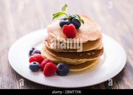 Pile de crêpes aux myrtilles et framboises pour le petit déjeuner sur table en bois. Banque D'Images