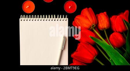 Tulipes rouges, carte vierge ou bloc-notes avec stylo et bougies isolées sur fond noir, espace de copie pour le texte Banque D'Images