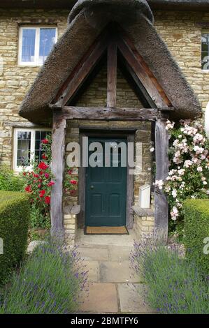 Porte avec une véranda de chaume inhabituelle soutenue sur des piliers en bois, dans le village d'Isham, Northamptonshire, Royaume-Uni Banque D'Images