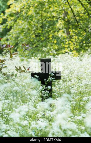 Croix de pierre ancienne ou crucifix dans un cimetière avec des fleurs sauvages. Espace de copie, vertical. Banque D'Images