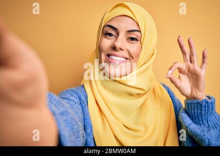 Jeune belle brune arabe femme portant hijab islamique faire selfie par caméra faisant signe ok avec les doigts, excellent symbole Banque D'Images