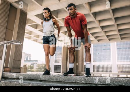 Homme et femme de fitness s'étendant ensemble à l'extérieur avant une course dans la ville. Deux personnes s'y sont sorties le matin en ville. Banque D'Images