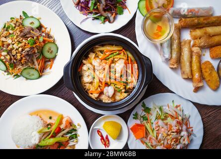 Dîner asiatique servi au restaurant.délicieux plats vietnamiens de mer dans la vue de dessus.Jambalaya avec crevettes, rouleaux de printemps et salades servis sur des assiettes blanches sur le t. Banque D'Images