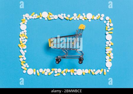 Chariot jaune dans le cadre de pilules blanches et capsules sur fond bleu pharmaceutique ou médical. Shopping pour la médecine en pharmacie, pharmacie Banque D'Images