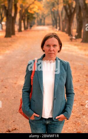 Portrait of businesswoman in autumn park, debout sur sentier entre les arbres avec un feuillage dynamique Banque D'Images