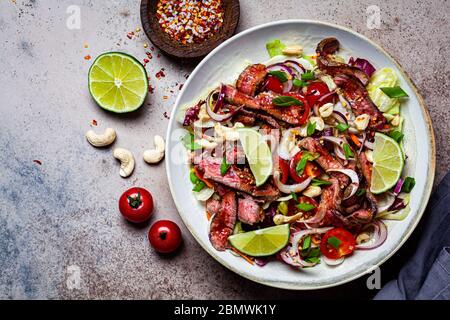 Salade de bœuf asiatique avec légumes et noix dans un bol blanc sur fond sombre. Concept alimentaire asiatique. Banque D'Images