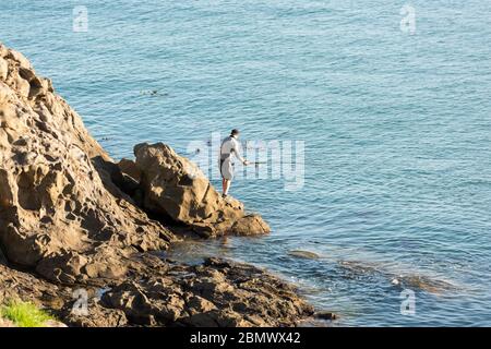 Un homme pêche en mer au large des roacks dans l'océan Pacifique Sud près de Katiki point Nouvelle-Zélande Banque D'Images