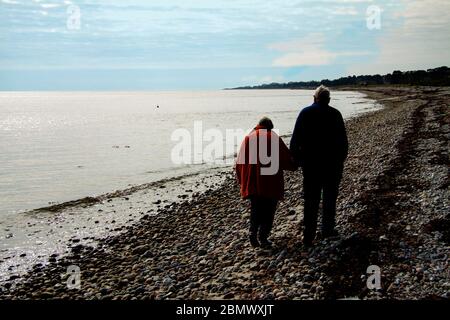 Couple âgé se promenant près de la mer en tenant les mains. Couple vu de derrière et en partie en silhouette. Banque D'Images